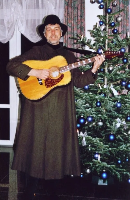 Gitarrist im Hirtenkostüm vor einem Weihnachtsbaum.