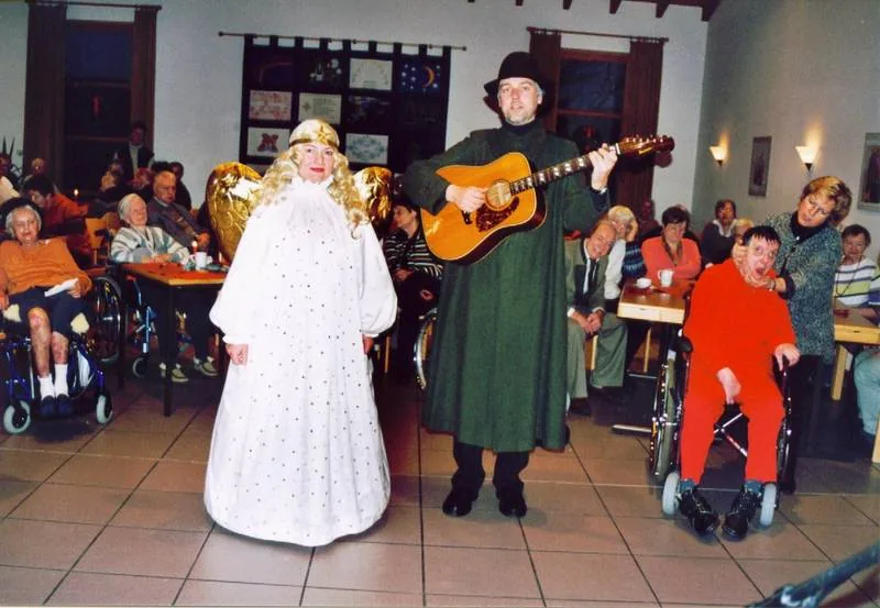 Wera als Engel und Bernd als Hirte mit Gitarre bei einem Weihnachtsauftritt vor Publikum.